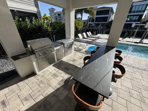 Large custom U-shaped outdoor kitchen with beautiful floating bar. Featuring built in Grill and Griddle as well as outdoor fridge. This large U-shaped custom outdoor kitchen features both a built in grill and griddle. As well as a large suspended bar and built in refrigerator.