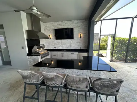 Large custom outdoor kitchen with stone veneer and polymer cabinets. Features a large bar with mounted TV. Custom outdoor kitchen with beautiful black granite countertops, a large L shaped bar and built in Grill and fridge.