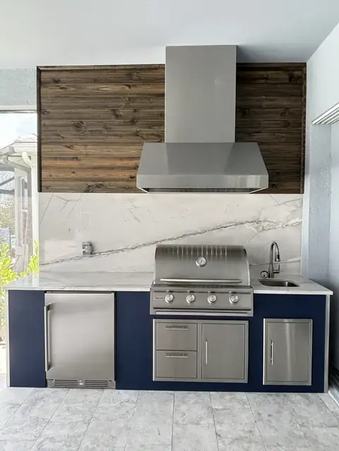 Polymer Cabinet outdoor kitchen with full heigh backsplash and tongue and groove accent wall. With Grill, Fridge and range hood. Blue marin grade polymer outdoor kitchen. Featuring a grill, fridge and range hood. Accented by a full height backsplash and tongue and groove accent wall.