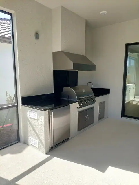 A simple outdoor kitchen with Granite backsplash built in Estero, FL with a grill, fridge and vent hood. A simple outdoor kitchen with Granite backsplash built in Estero, FL with a grill, fridge and vent hood.