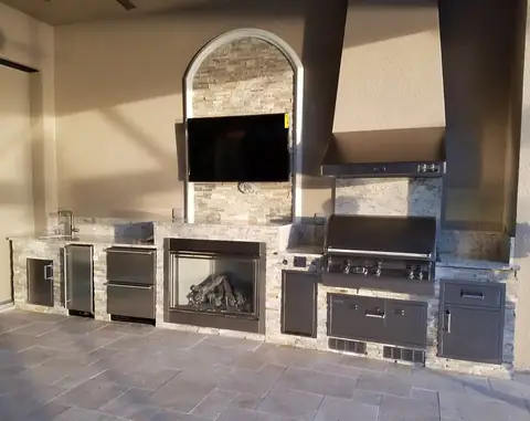 An ornate outdoor kitchen built Naples, FL with a built in fireplace and mounted TV. An ornate outdoor kitchen built Naples, FL with a built in fireplace and mounted TV.