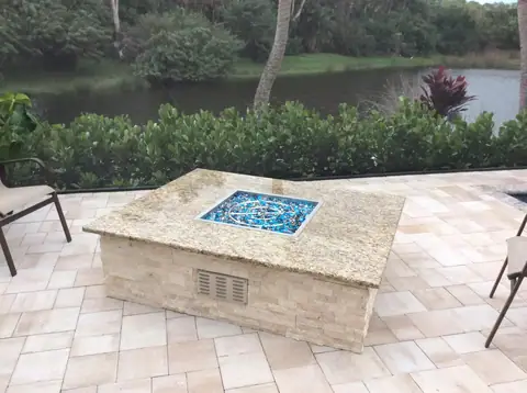 Custom built standalone outdoor firepit with granite top and stack stone surround in Naples, FL. Custom built standalone outdoor firepit on pavers in a lanai with granite top and stack stone surround in Naples, FL.