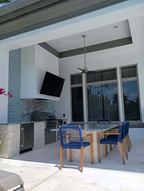 A custom outdoor kitchen with hood surround and mounted TV in Bonita Springs, FL. A large custom outdoor kitchen with hood surround and mounted TV, as well as a large custom island in Bonita Springs, FL.
